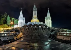 Bazilika Notre-Dame du Rosaire zalitá světlem po setmění, korunní kupole se leskne nad náměstím